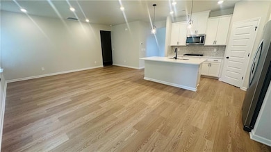 Kitchen with appliances with stainless steel finishes, light wood finished floors, decorative backsplash, and open floor plan