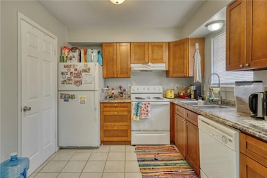 Kitchen featuring white appliances, light tile patterned flooring, and brown cabinets