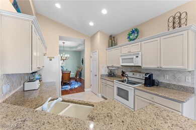 Kitchen with lofted ceiling, light tile patterned floors, an inviting chandelier, white appliances, and a sink