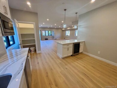 Kitchen featuring open floor plan, white cabinetry, light stone countertops, pendant lighting, and wine cooler