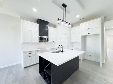 Kitchen featuring a center island with sink, sink, white cabinetry, decorative light fixtures, and light hardwood / wood-style floors