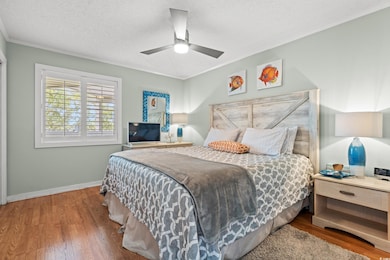 Bedroom featuring a textured ceiling, wood finished floors, crown molding, and a ceiling fan
