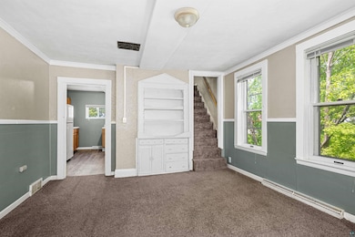 Unfurnished bedroom with a baseboard radiator, fridge, carpet, ornamental molding, and baseboards