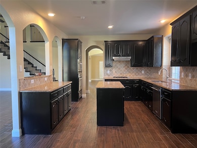 Kitchen with dark cabinets, light stone countertops, backsplash, and recessed lighting