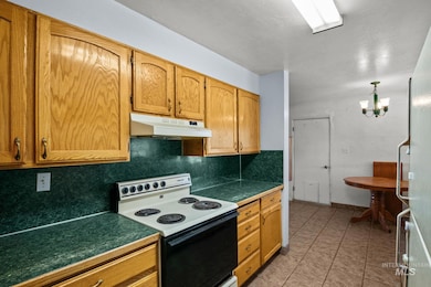 Kitchen with range with electric stovetop, tasteful backsplash, under cabinet range hood, freestanding refrigerator, and light tile patterned flooring