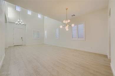 Spare room featuring a chandelier, light wood-style floors, and a towering ceiling