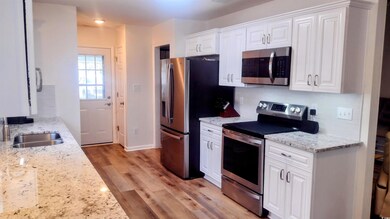 Kitchen with appliances with stainless steel finishes, white cabinetry, light wood-style flooring, backsplash, and light stone countertops