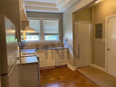 Kitchen with white appliances, electric panel, tasteful backsplash, white cabinets, and light countertops