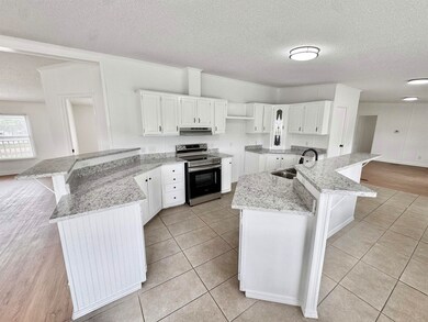 Kitchen with stainless steel electric range oven, a textured ceiling, a peninsula, a sink, and under cabinet range hood