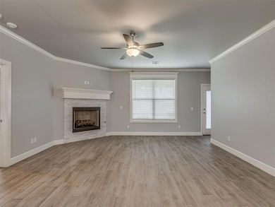 Unfurnished living room with ceiling fan, wood finished floors, baseboards, and ornamental molding