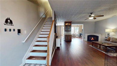 Stairs featuring ceiling fan, wood finished floors, a warm lit fireplace, and a textured ceiling