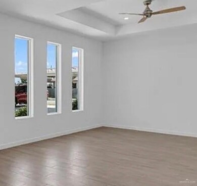 Empty room featuring a raised ceiling, wood finished floors, and ceiling fan