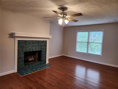 Unfurnished living room featuring a fireplace, wood finished floors, a textured ceiling, and ceiling fan