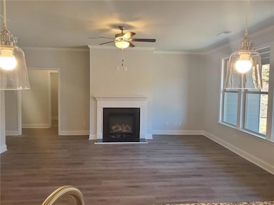 Unfurnished living room featuring crown molding, dark wood-style floors, a fireplace with flush hearth, and a ceiling fan