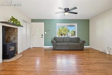 Living room with a wood stove, light wood-style flooring, and ceiling fan