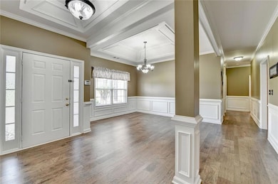 Foyer with a chandelier, decorative columns, wood finished floors, a decorative wall, and a wainscoted wall