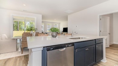 Kitchen with stainless steel dishwasher, a sink, open floor plan, light countertops, and light wood finished floors