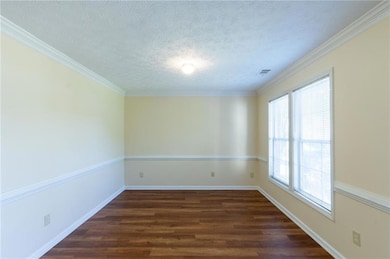 Spare room with healthy amount of natural light, dark wood finished floors, a textured ceiling, baseboards, and crown molding