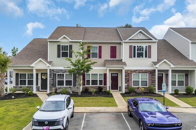 Townhome / multi-family property with stone siding, a shingled roof, uncovered parking, and a front yard