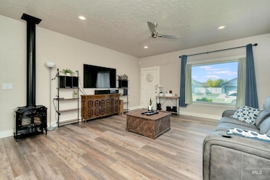 Living room with a wood stove, light wood-style flooring, ceiling fan, a textured ceiling, and recessed lighting