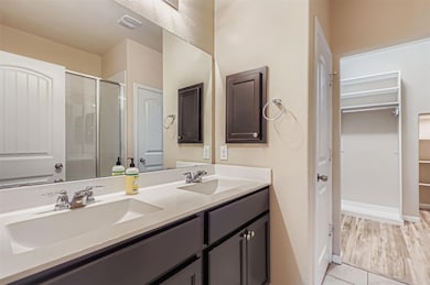 Bathroom featuring a walk in closet, double vanity, a stall shower, and light tile patterned flooring