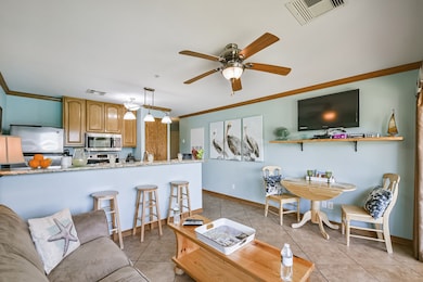 Cozy dining nook with a small wooden table and two chairs, featuring a wall-mounted TV and decorative shelf. Large glass doors open to a balcony with outdoor seating, offering a pleasant view and natural light.