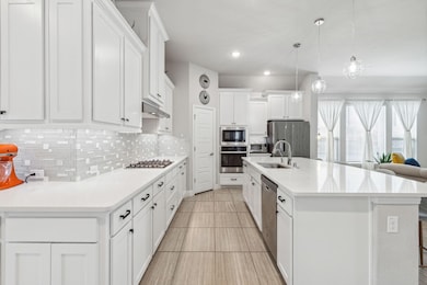 Kitchen featuring appliances with stainless steel finishes, decorative light fixtures, a center island with sink, and white cabinets