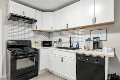 Kitchen with black appliances, a sink, under cabinet range hood, light countertops, and white cabinets