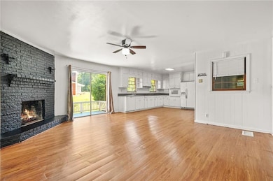Unfurnished living room featuring a ceiling fan, light wood finished floors, and a fireplace