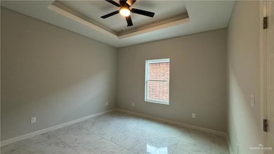 Tiled empty room featuring ceiling fan and a tray ceiling