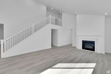 Unfurnished living room with a high ceiling, light wood finished floors, stairway, a glass covered fireplace, and recessed lighting