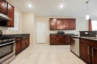 Kitchen featuring stainless steel appliances, hanging light fixtures, dark stone counters, under cabinet range hood, and recessed lighting