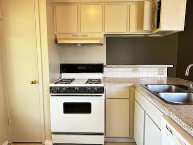 Kitchen with white appliances, light countertops, under cabinet range hood, and cream cabinetry