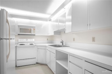 Kitchen with white appliances, a sink, light countertops, and white cabinetry