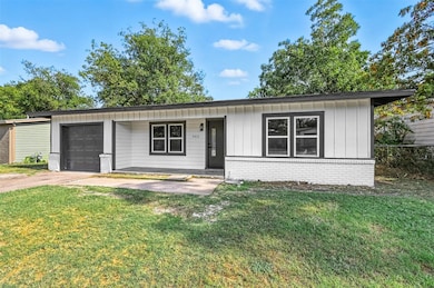 View of front of house featuring a garage, brick siding, board and batten siding, a front lawn, and driveway