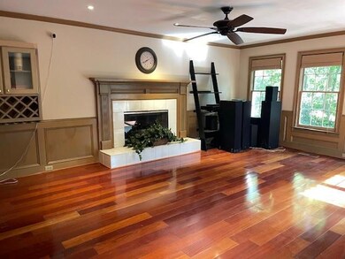 Unfurnished living room with ornamental molding, wood finished floors, a wainscoted wall, a fireplace, and ceiling fan