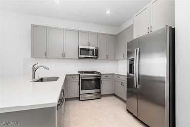 Kitchen with appliances with stainless steel finishes, gray cabinetry, a sink, a peninsula, and light tile patterned floors