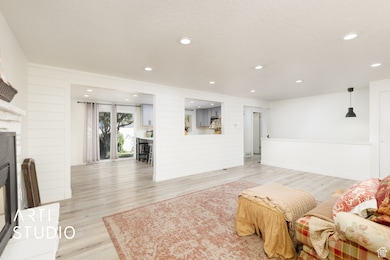 Living area featuring light wood-type flooring, a fireplace with raised hearth, recessed lighting, a textured ceiling, and wood walls