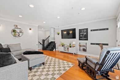Living room with ornamental molding, light wood finished floors, recessed lighting, and stairs