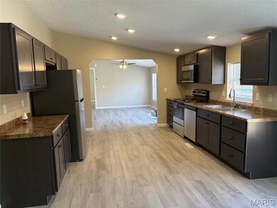 Kitchen featuring dark countertops, arched walkways, ceiling fan, appliances with stainless steel finishes, and a textured ceiling