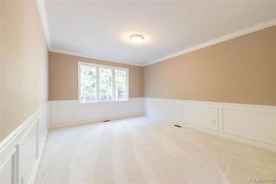 Empty room with crown molding, a decorative wall, wainscoting, and light colored carpet