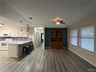 Kitchen featuring light hardwood / wood-style floors, kitchen peninsula, white appliances, a breakfast bar area, and white cabinetry