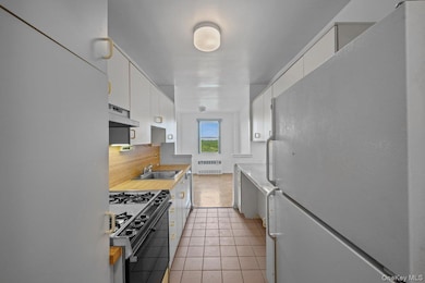 Kitchen featuring freestanding refrigerator, black range with gas cooktop, radiator, under cabinet range hood, and tasteful backsplash