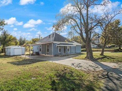 Rear view of house featuring a lawn, an outdoor structure, a garage, roof with shingles, and driveway
