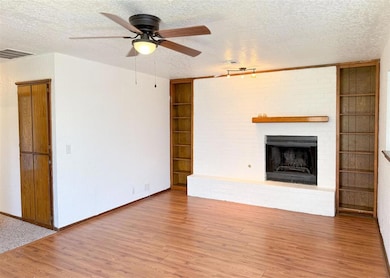 Unfurnished living room featuring built in shelves, a textured ceiling, a fireplace, wood finished floors, and a ceiling fan
