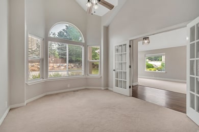 Carpeted empty room with high vaulted ceiling, french doors, and ceiling fan