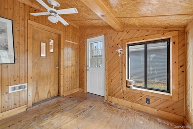 Entryway with wood walls, hardwood / wood-style floors, beam ceiling, and a ceiling fan