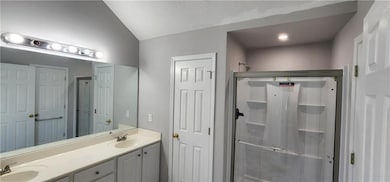 Full bath featuring a shower stall, lofted ceiling, and double vanity