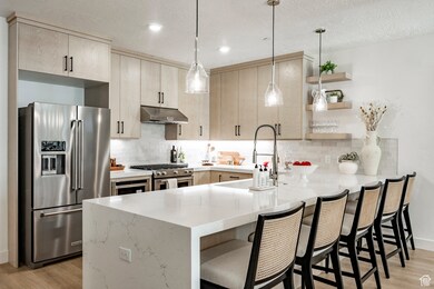Kitchen featuring a peninsula, premium appliances, light wood-type flooring, a breakfast bar, and a textured ceiling