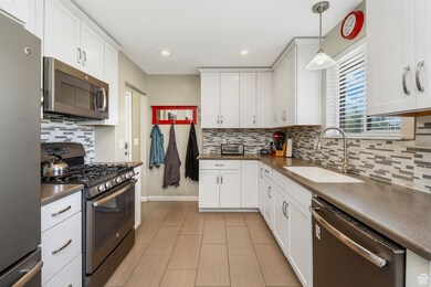 Kitchen featuring stainless steel appliances, dark countertops, white cabinets, hanging light fixtures, and tasteful backsplash